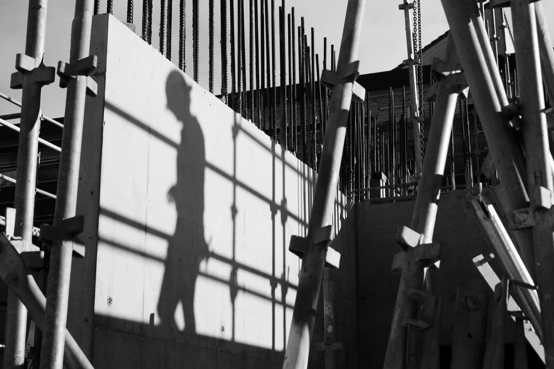 Silhouette of a worker cast on concrete formwork among reinforcement steel on a live construction site